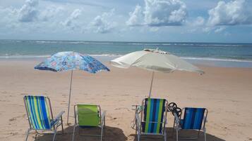 Una playa con tres sillas y dos sombrillas.