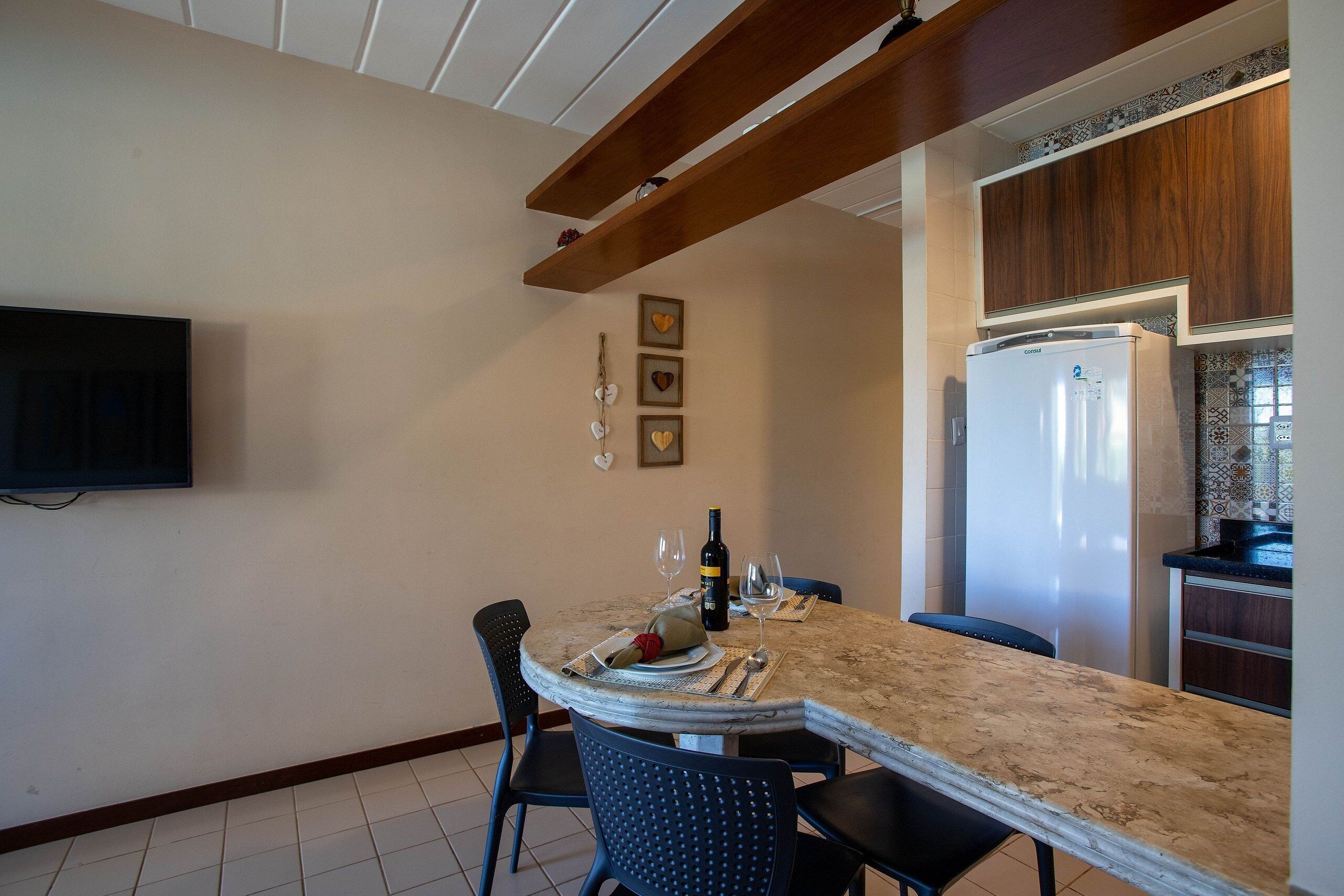 A kitchen with a dining area, a refrigerator, and a television mounted on the wall.