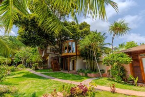 A modern house with a circular glass structure, surrounded by lush greenery and palm trees. - Rocks Beach Boutique Bungalows (Phu Quoc)