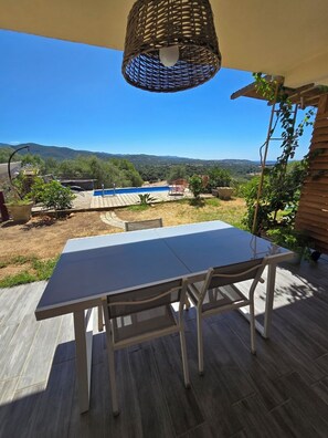 An outdoor patio with a table and chairs, a hanging light fixture, and a view of a pool and mountains. - One-bedroom apartment on the garden level of a villa, in a quiet location, with a pool and views of the sea and mountains. (Bastelicaccia)