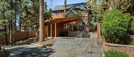 A wooden cabin with a stone foundation, surrounded by tall trees and a wooden deck.