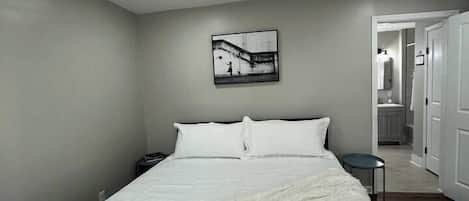 Ein Schlafzimmer mit einem großen Bett, einem Nachttisch, einem Wandbild und einer Tür zu einem Badezimmer.