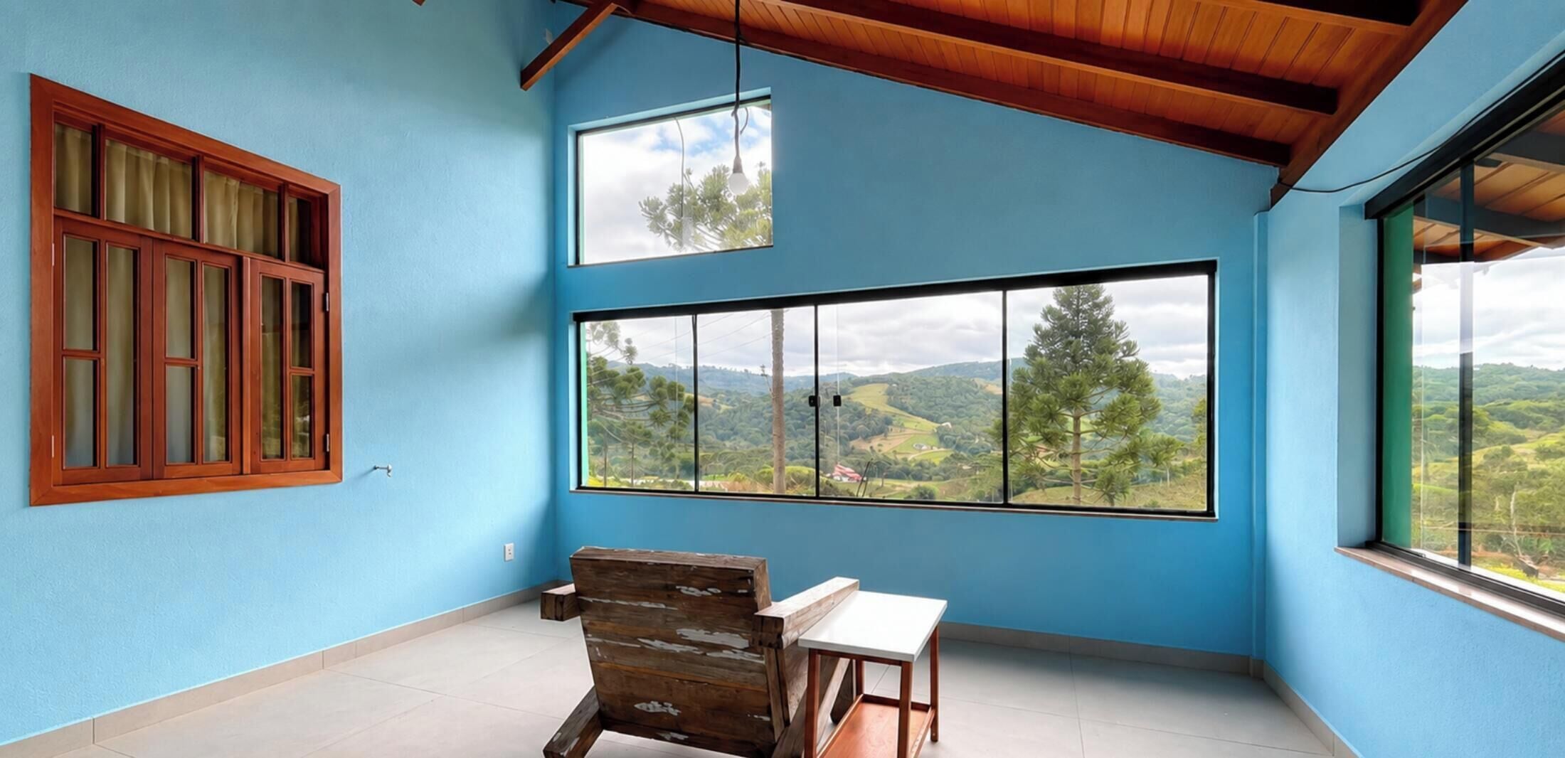 A room with a large window offering a view of a hilly landscape, a wooden chair, and a small table.