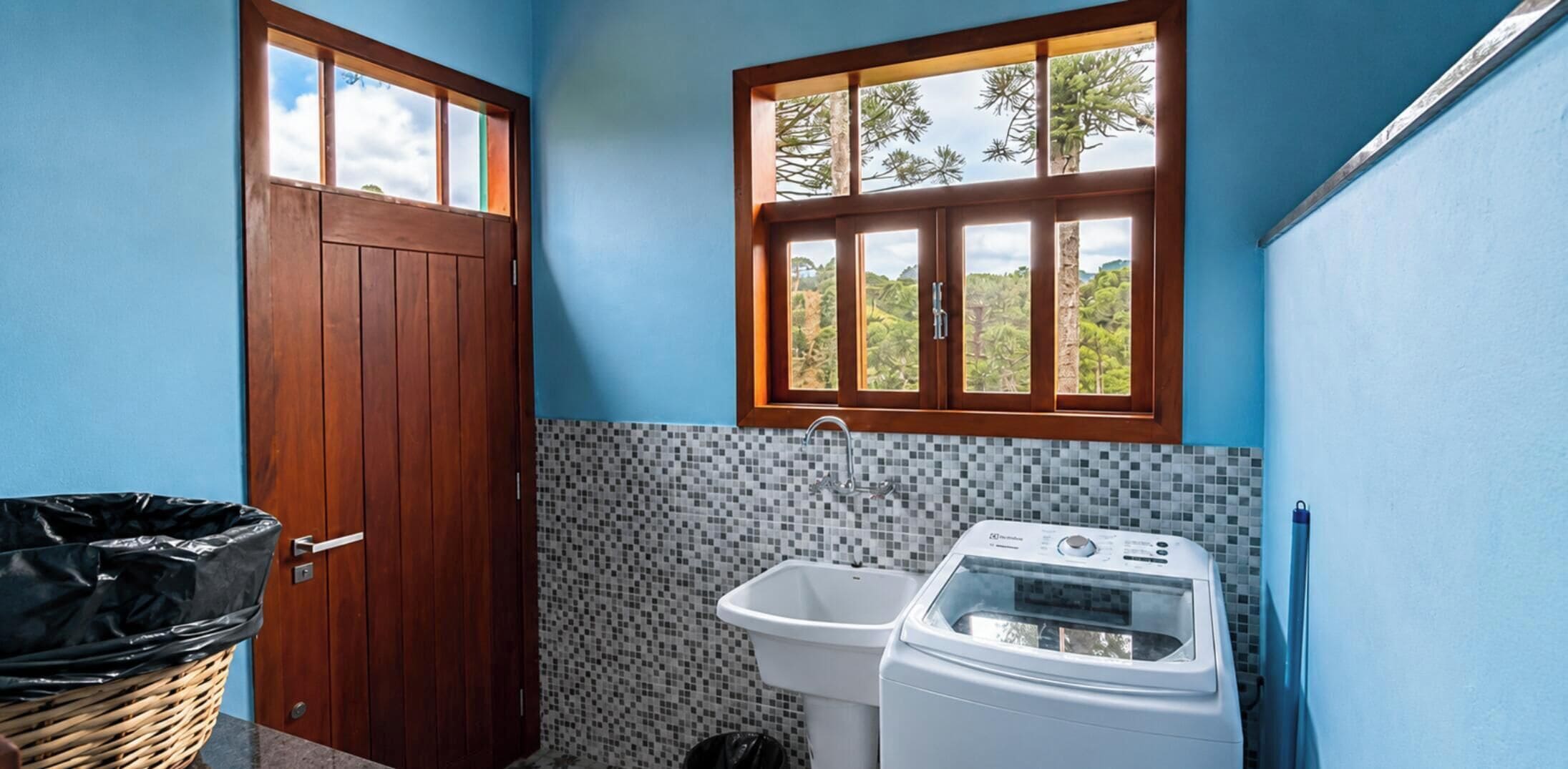 A small bathroom with a wooden door, a window, a tiled backsplash, a sink, and a washing machine.