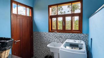 A small bathroom with a wooden door, a window, a tiled backsplash, a sink, and a washing machine.