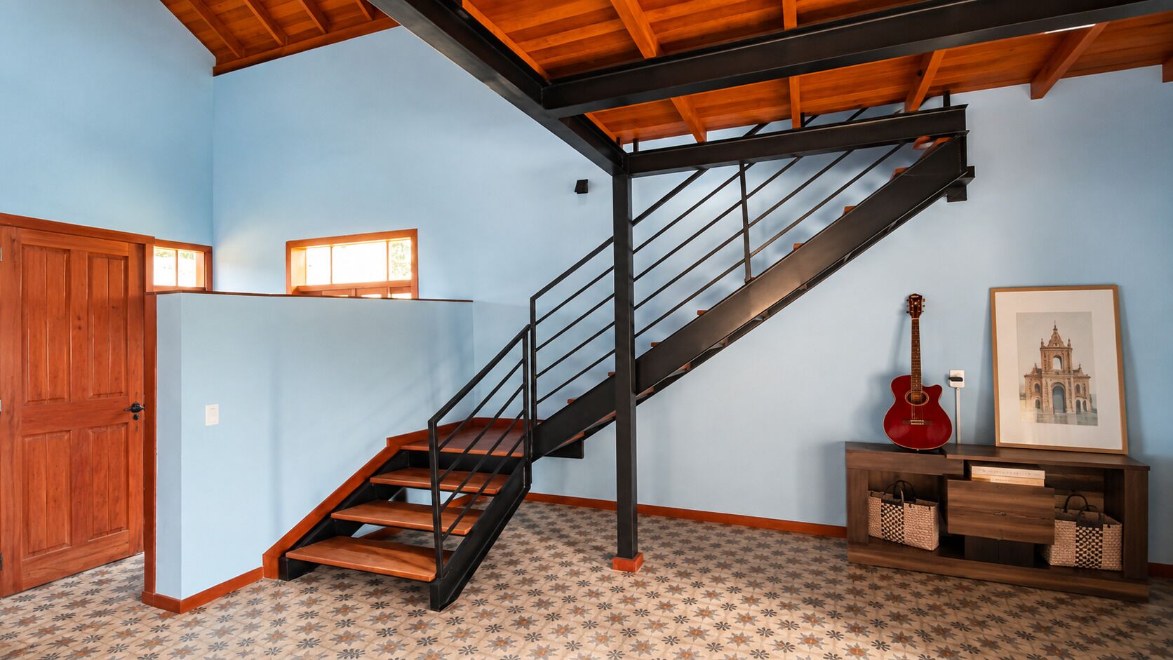 A staircase with a wooden finish and metal railings, leading to a landing with a door and a window.