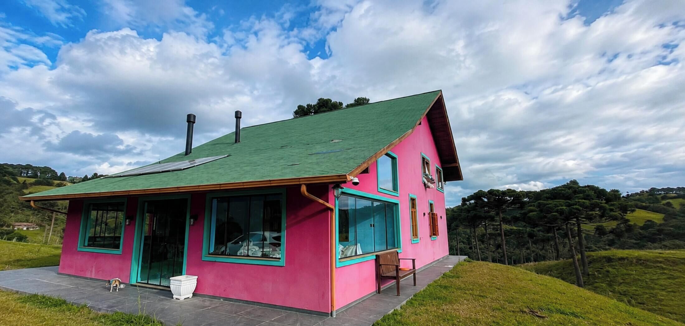 Uma casa rosa com telhado verde, varanda e vista para a paisagem ao redor.