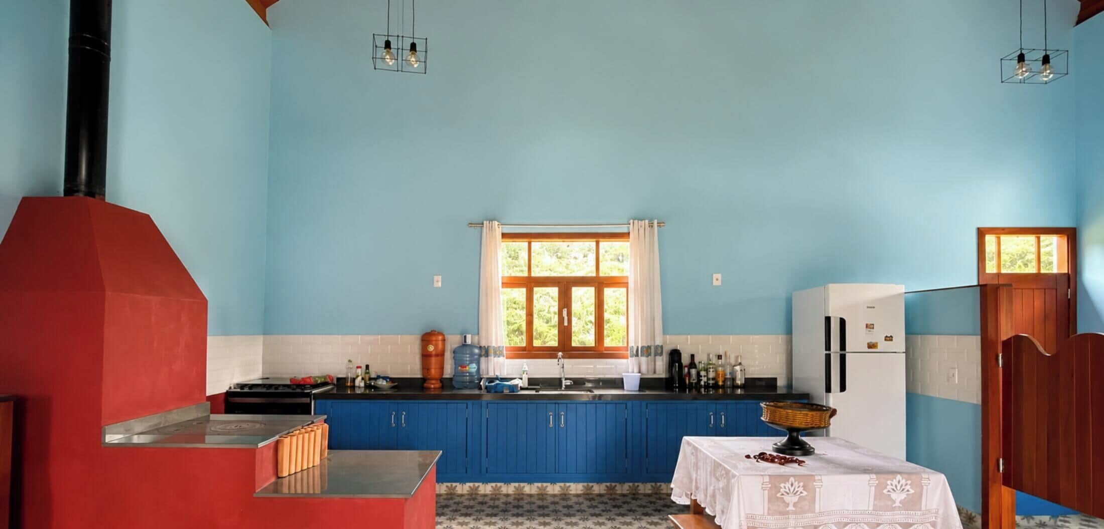 A kitchen with blue cabinets, a stove, a refrigerator, and a window with curtains.