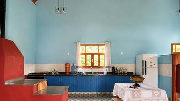A kitchen with blue cabinets, a stove, a refrigerator, and a window with curtains.