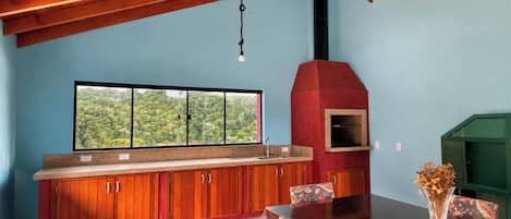 Una cocina con alacenas de madera, un horno rojo y una ventana con vistas al verdor.