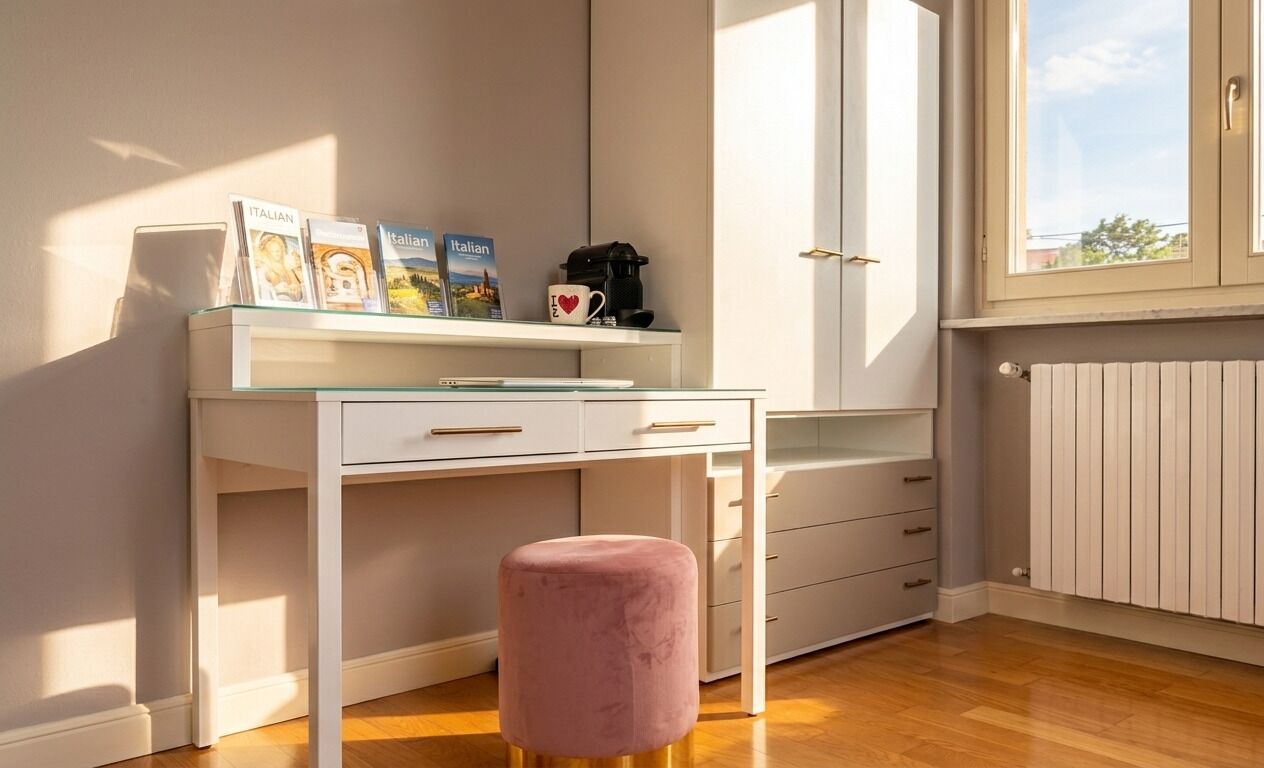 Ein Zimmer mit einem weißen Schreibtisch, einem pinken Hocker und einem Fenster mit Jalousien.