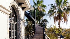 A staircase leading to a balcony with a view of palm trees. - Cabo San Lucas Castle · Rooftop Sea Views (Cabo San Lucas)