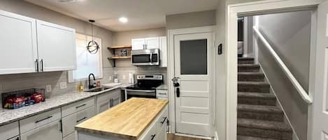 A modern kitchen with white cabinets, a wooden countertop, and a built-in microwave.