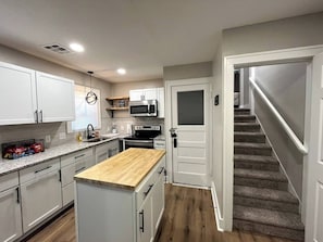 Una cocina moderna con armarios blancos, encimera de madera y microondas integrado.