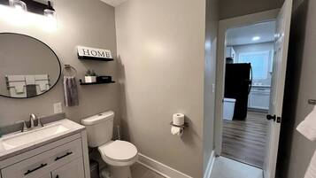 Ein Badezimmer mit Toilette, Waschbecken und Spiegel. Über dem Spiegel hängt ein Schild mit der Aufschrift 'HOME' und eine Handtuchstange ist an der Wand befestigt.