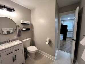 Un baño con inodoro, lavabo y espejo. Hay un letrero que dice 'HOME' sobre el espejo y un perchero en la pared.