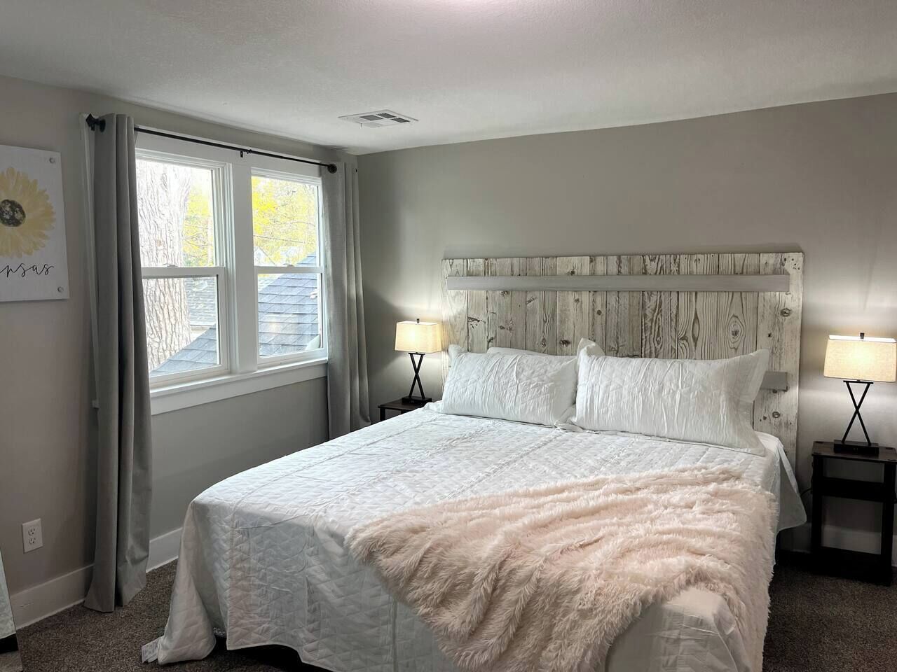 Quarto com cama, duas mesas de cabeceira, janela com cortinas e cabeceira.