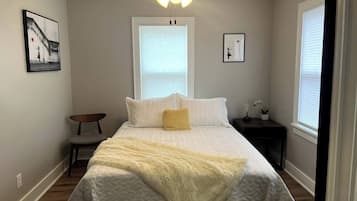 Ein Schlafzimmer mit einem Bett, Deckenventilator, Fenster, Nachttisch und einem Sessel.