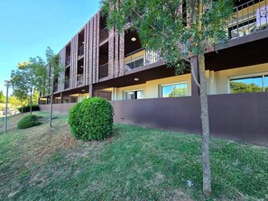 Un immeuble à plusieurs étages doté de balcons, d’une pelouse bien entretenue et d’arbres adultes.