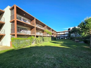 Un immeuble résidentiel à plusieurs étages, doté de balcons, d’une pelouse bien entretenue et entouré de verdure.