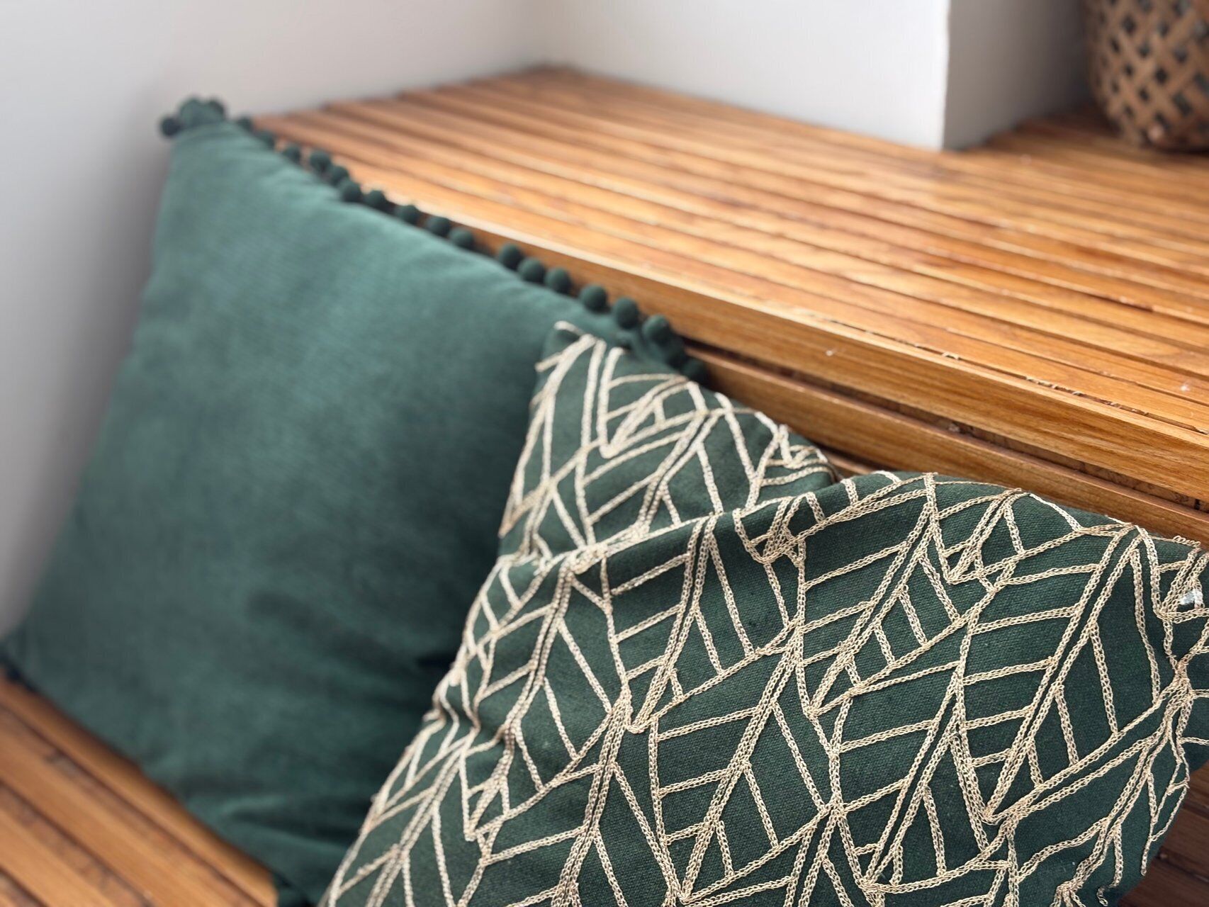 Un banc de fusta amb coixí verd i un coixí estampat.