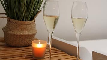 Dos copas de vino blanco sobre una mesa de madera con una vela y una planta en maceta.