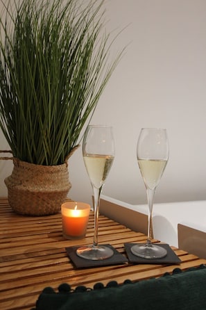 Two glasses of white wine on a wooden table with a candle and a potted plant.