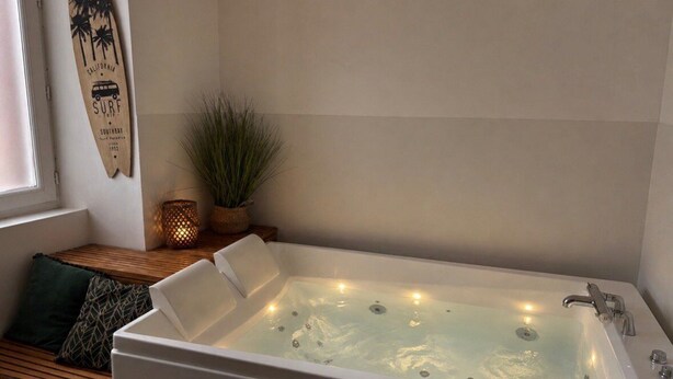 Een moderne badkamer met een groot bad, een houten bankje, een surfboard decoratie en een potplant.