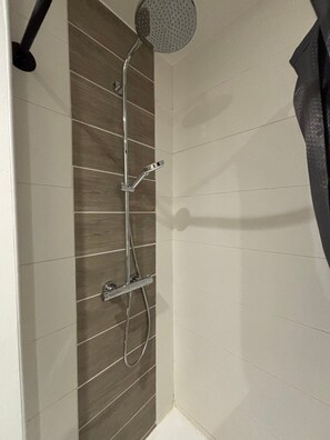 A shower with a handheld showerhead and a wall-mounted faucet.