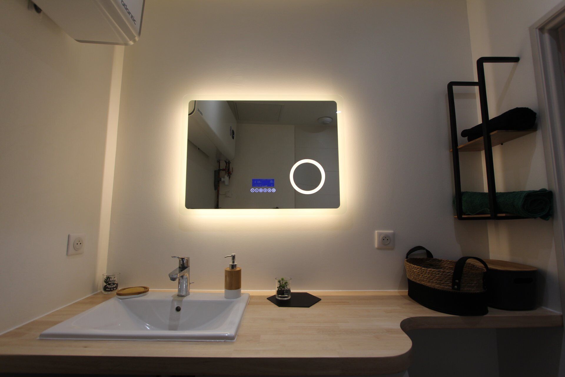 A bathroom with a white sink, a mirror with a light, a shelf with a towel, and a basket.