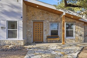 A stone facade with a wooden door and windows, a bench, and a stone-paved entrance. - Craftsman style lake cottage family & pet friendly (Austin)
