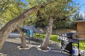 Un jardin avec un barbecue, une table et des chaises, et une clôture en bois.