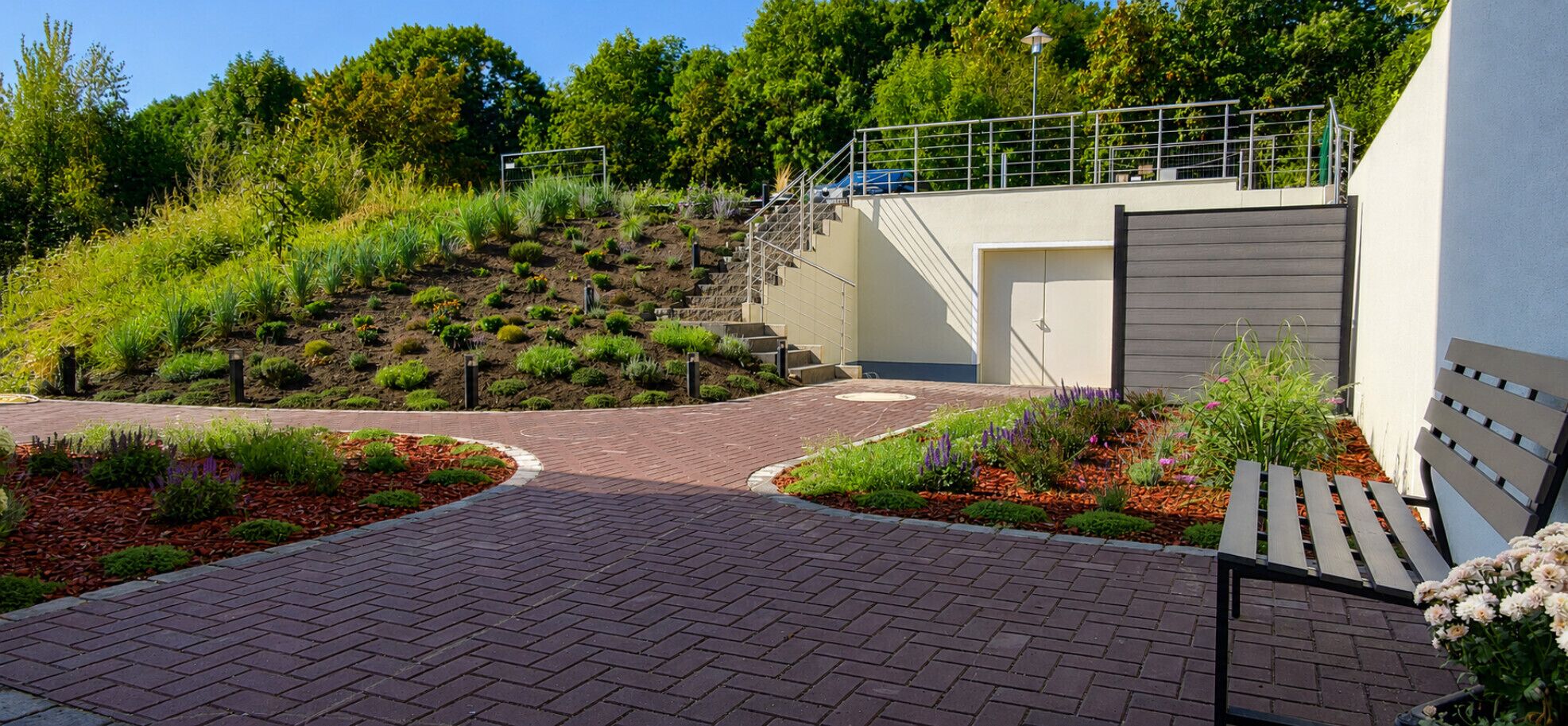 A paved entrance with a brick pathway leading to a building with a grey exterior and a metal staircase.