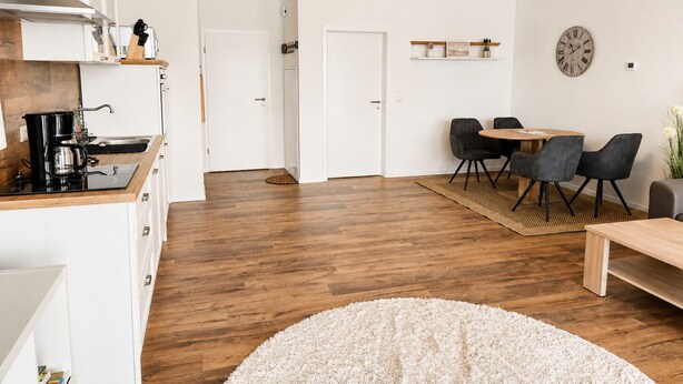 Une cuisine moderne équipée d’une machine à café, d’un coin repas avec une table et des chaises, et d’une horloge au mur.