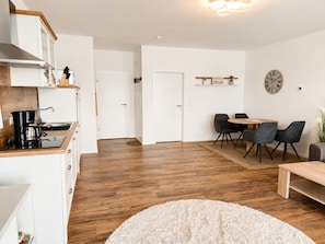 A modern kitchen with a coffee maker, a dining area with a table and chairs, and a clock on the wall. - Spacious 60 m² vacation rental with 2 balconies, lake views, right on the water, and a boat dock (Neukieritzsch)
