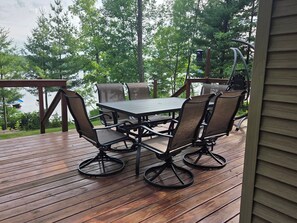 Une terrasse en bois avec une table et des chaises, donnant sur une étendue d’eau et entourée d’arbres.