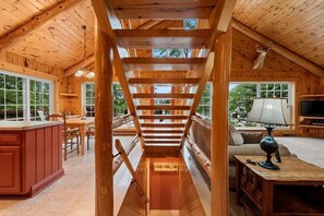 A wooden interior with a central staircase, a kitchen area, and a living space with a television.