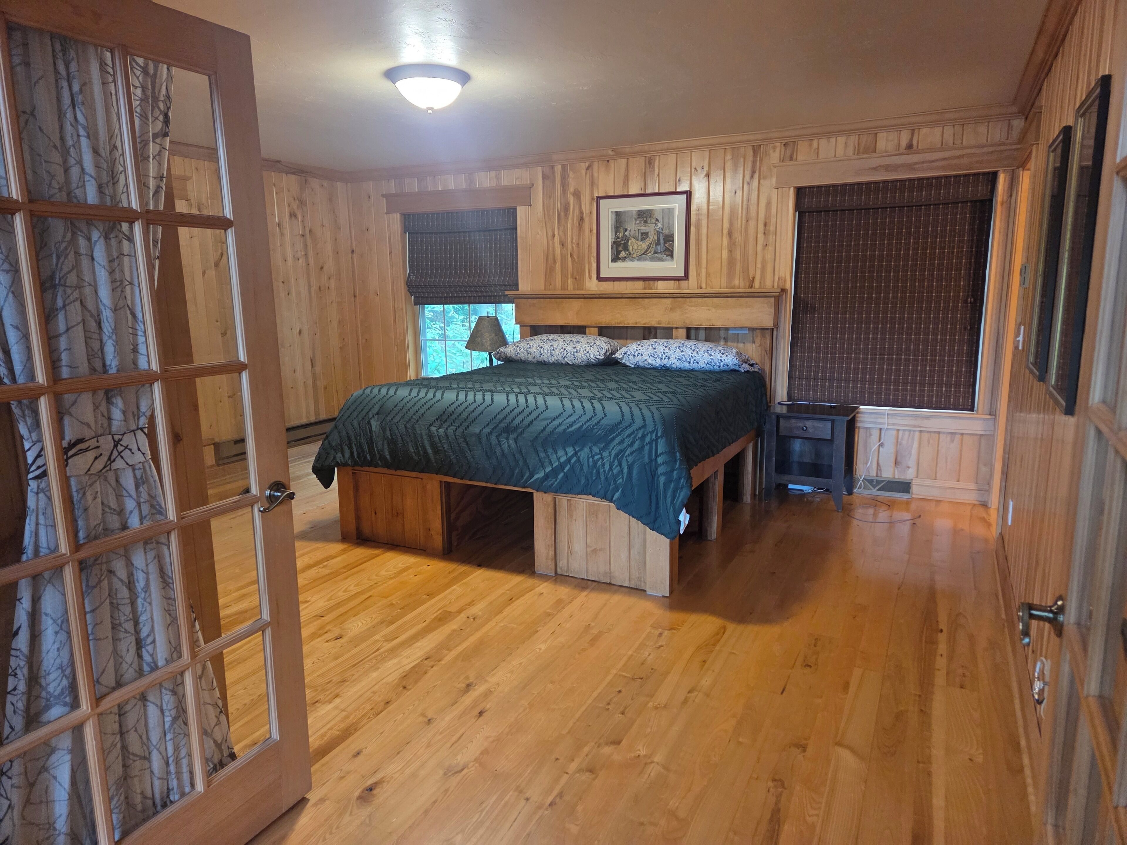 Une chambre à coucher aux murs lambrissés, avec un lit, une table de chevet et une fenêtre avec des rideaux.