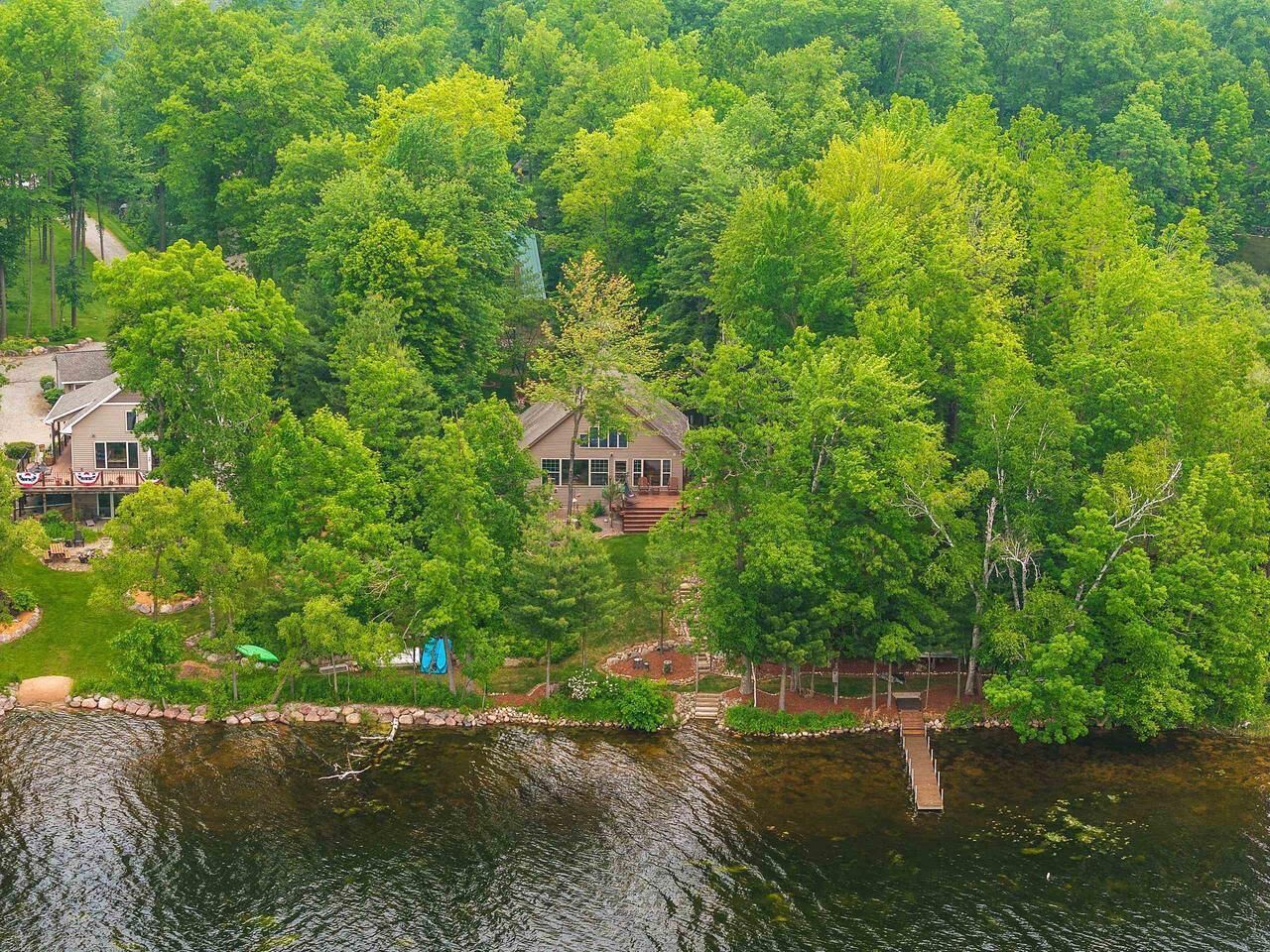 Une maison entourée d’une forêt dense, un quai et un petit bateau.