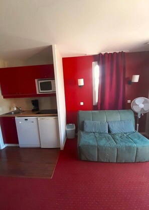 A compact room with a kitchenette, a bed, and a fan.