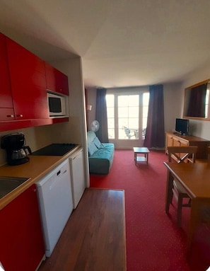 A compact living space with a kitchenette, a sofa, a dining table, and a television.