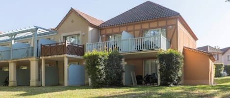 A two-story residential building with a balcony, a covered patio, and a well-maintained lawn.