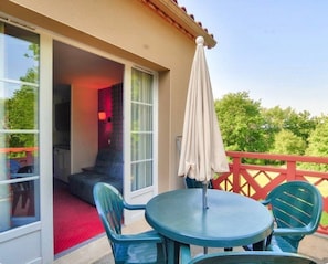 A balcony with a table and chairs, a sliding glass door leading to an interior room, and a red railing.