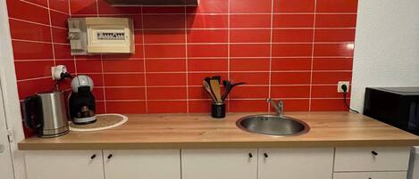 Une cuisine avec des meubles blancs, un plan de travail en bois, un évier en acier inoxydable et un dosseret carrelé de carreaux rouges.