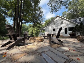 A cabin with a stone patio, Adirondack chairs, and a wooden deck.