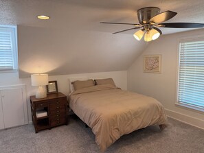 A bedroom with a bed, a nightstand, a ceiling fan, and a radiator.