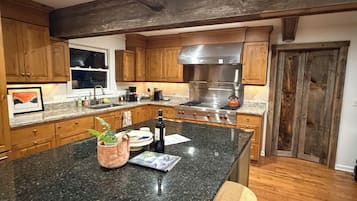 Une cuisine avec des meubles en bois, un plan de travail en granit, une cuisinière en acier inoxydable et un tabouret en bois.