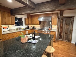 A kitchen with wooden cabinets, a granite countertop, a stainless steel stove, and a wooden stool.