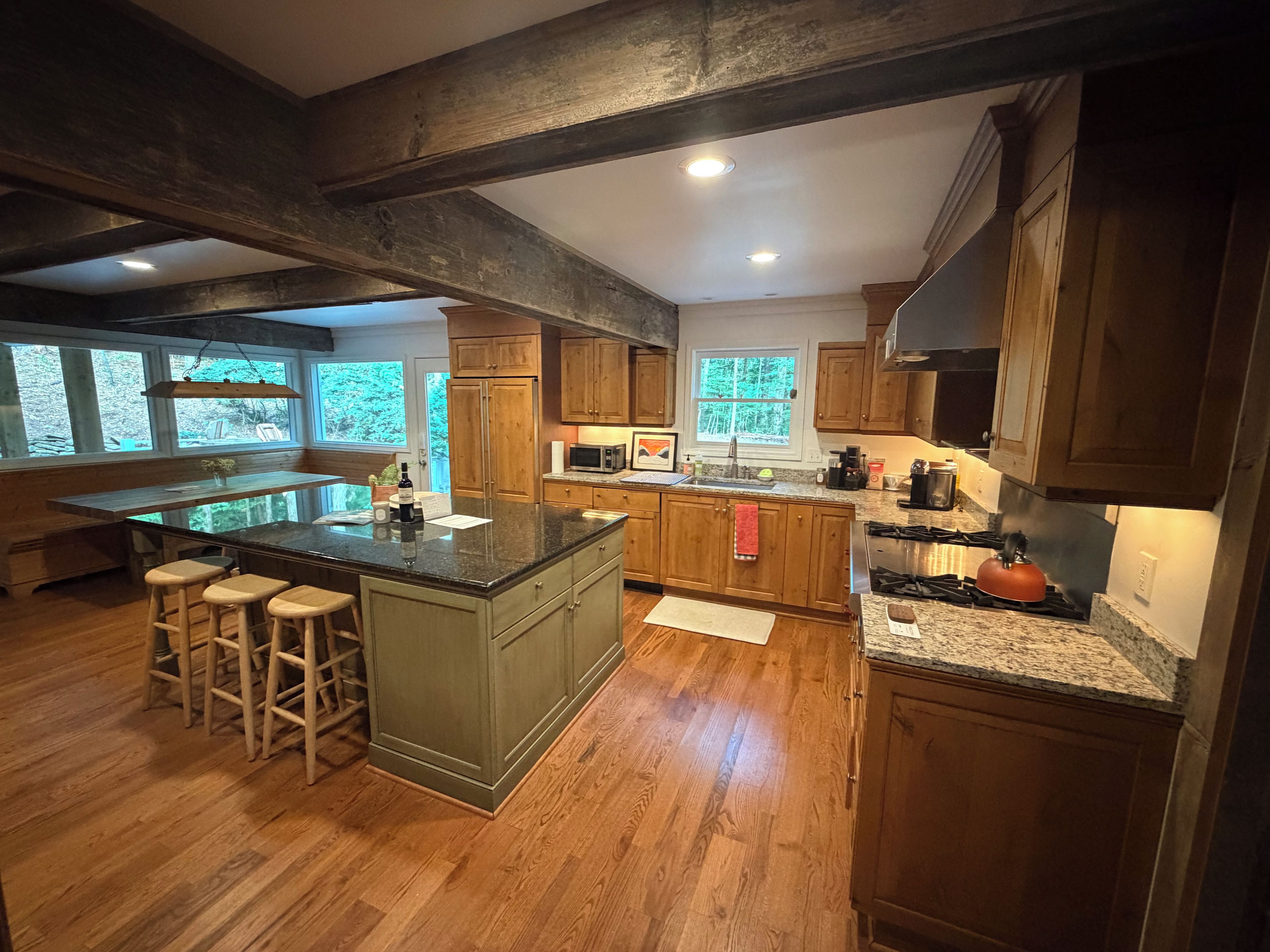 A spacious kitchen with wooden cabinets, a large island with stools, and a view of the outdoors through large windows.