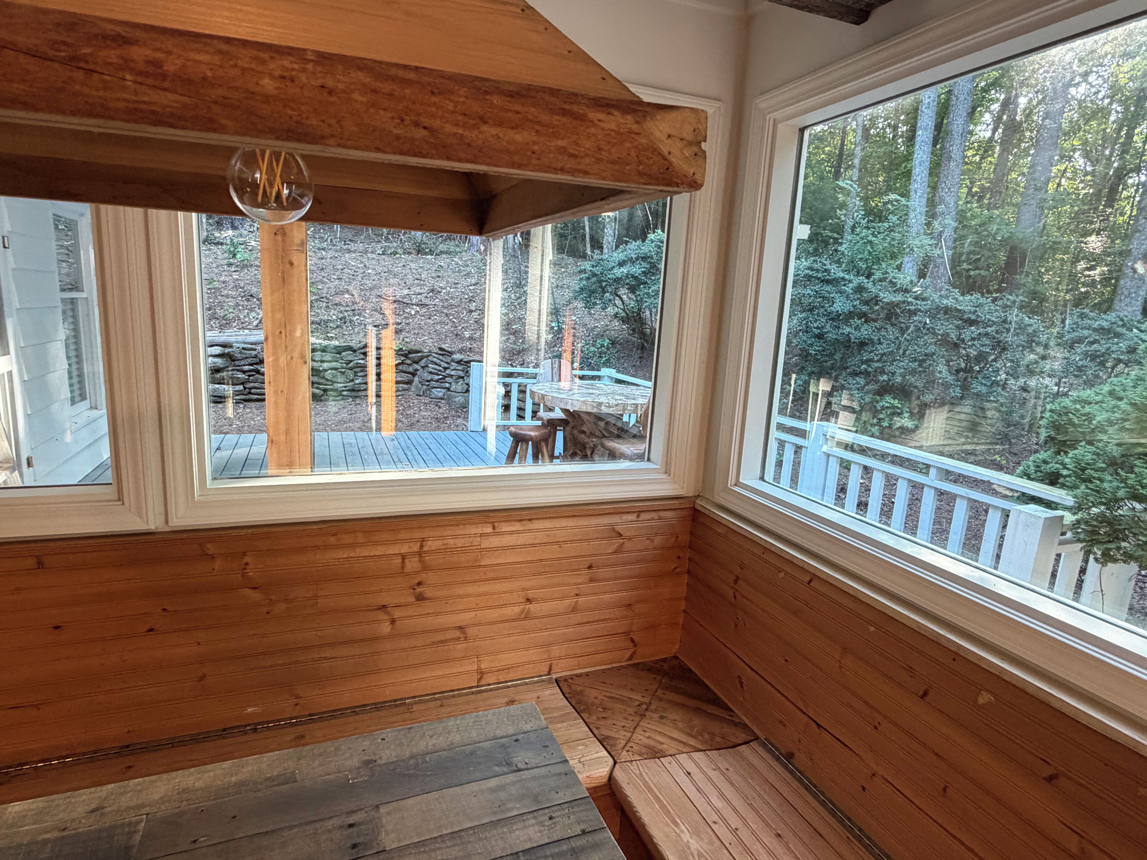 A room with wooden walls and large windows overlooking a deck and forest.